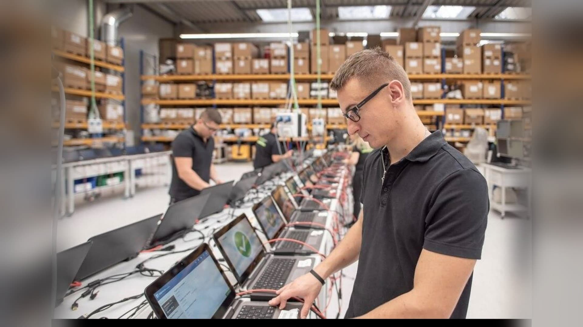 Técnico da Brain na bancada de preparação, testando uma fileira de notebooks com o teste de segurança aprovado nas telas