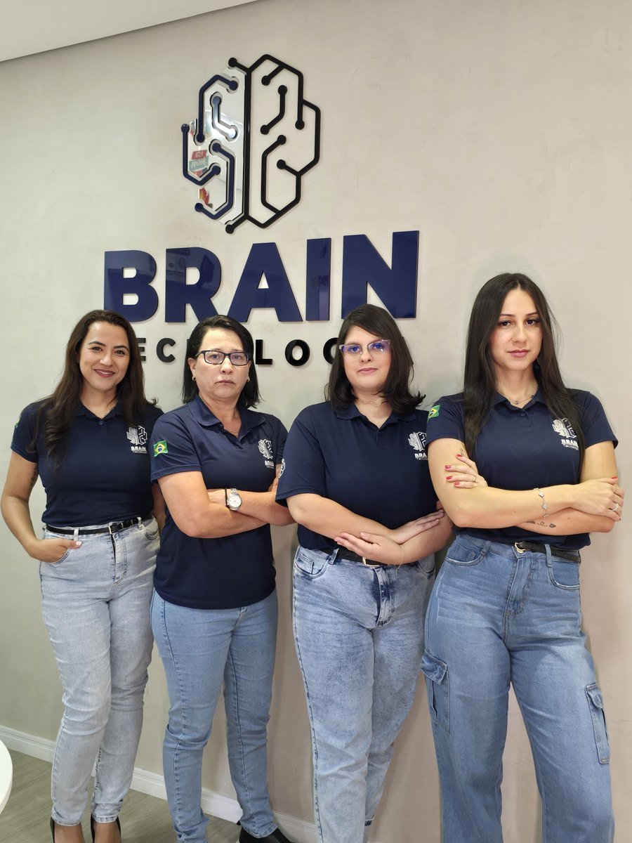 Quatro colaboradoras da Brain de uniforme em frente à parede com a marca