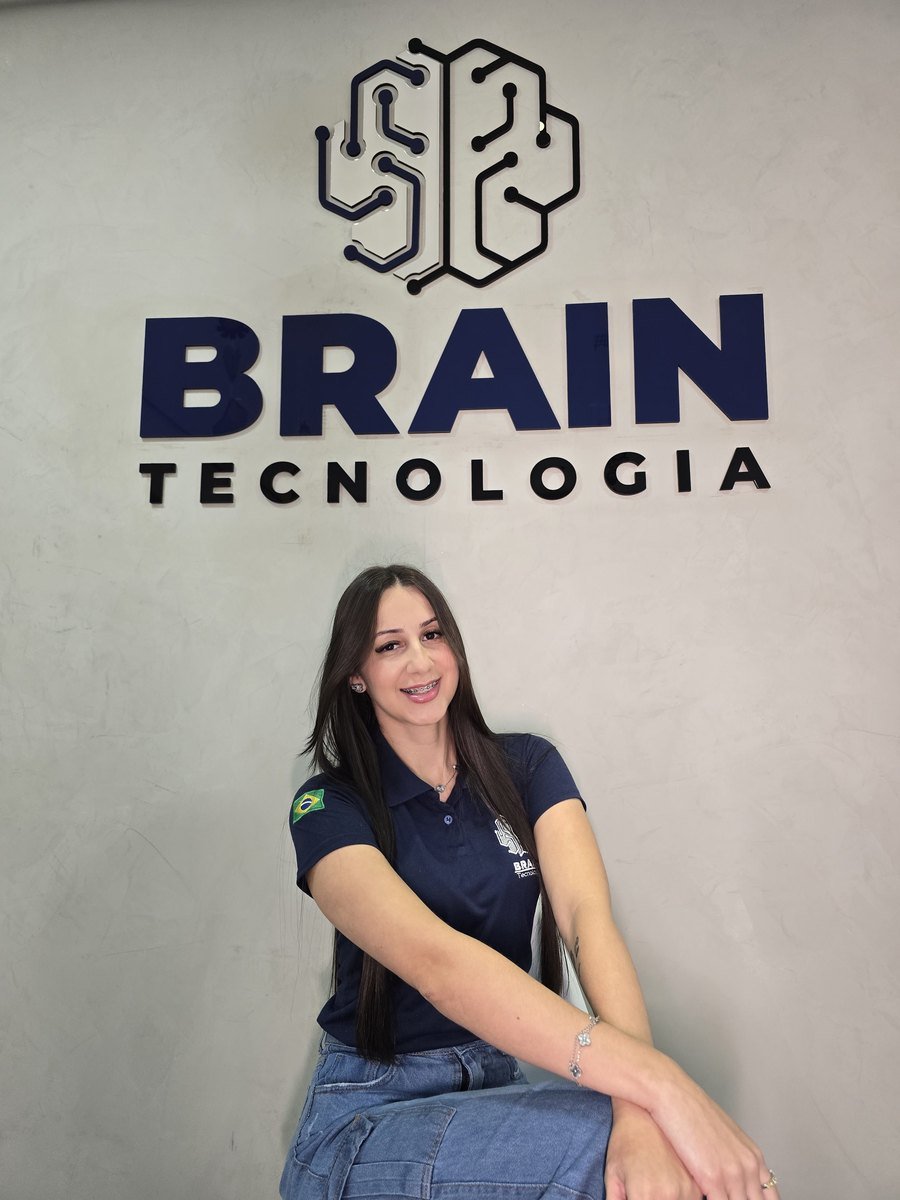 Colaboradora da Brain de uniforme em frente à parede com a marca